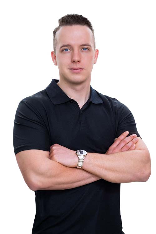 Mann mit neutralem Gesichtsausdruck, schwarzem Poloshirt, verschränkten Armen, weißer Uhr.